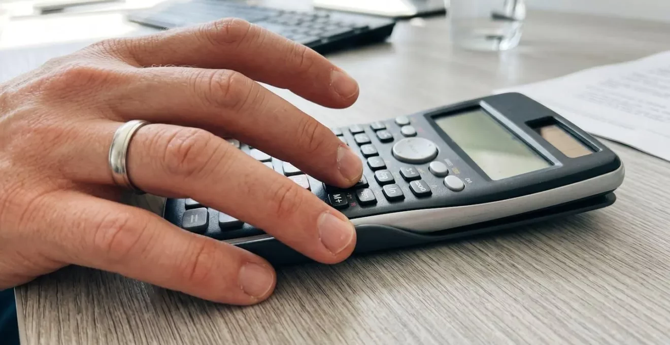 Gros plan sur une main utilisant une calculatrice moderne posée sur un bureau avec des documents financiers flous en arrière-plan